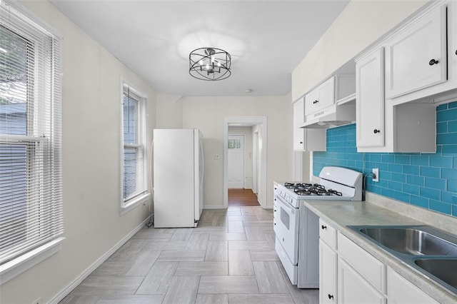 kitchen with white appliances, under cabinet range hood, white cabinets, and a chandelier
