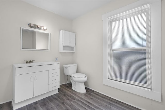 half bathroom with toilet, wood finished floors, vanity, and baseboards