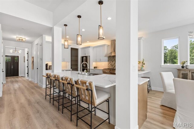 401 Rayburn Ave, Sunset Hills, MO 63127 - kitchen with a sink, wall chimney range hood, a kitchen bar, a chandelier, and light wood-type flooring