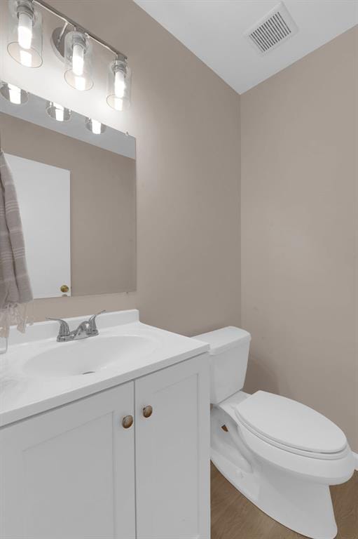half bath featuring toilet, wood finished floors, and vanity
