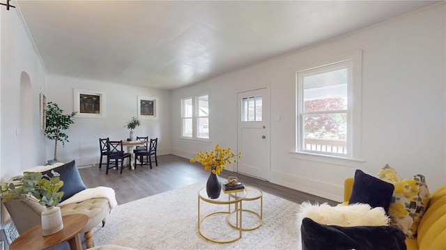 living room with healthy amount of natural light, wood finished floors, arched walkways, baseboards, and crown molding