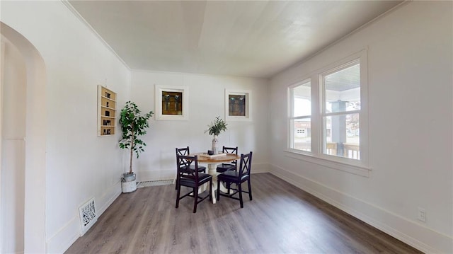dining area featuring arched walkways, wood finished floors, baseboards, and crown molding
