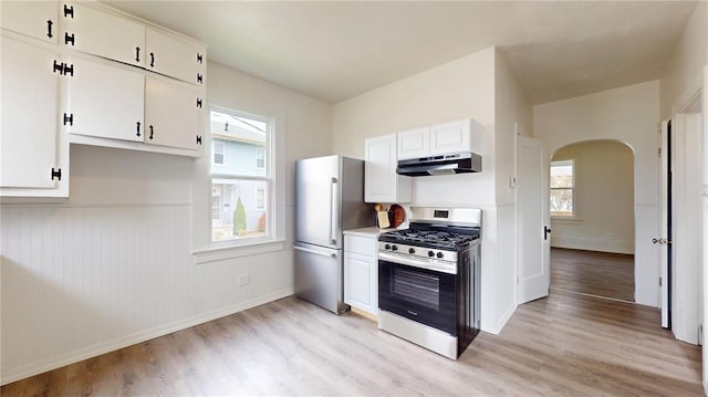 kitchen with stainless steel appliances, under cabinet range hood, arched walkways, and light wood finished floors