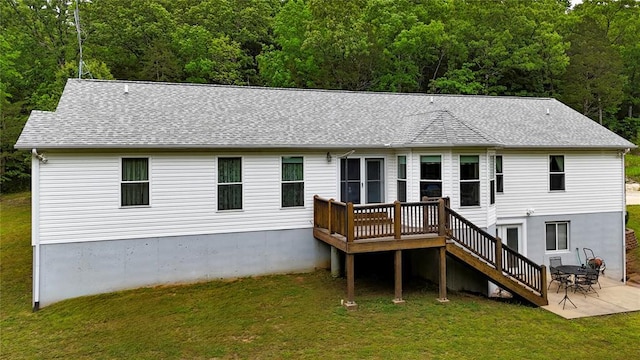 rear view of house featuring a wooded view, a lawn, a deck, and a shingled roof