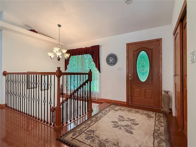 foyer entrance featuring a chandelier, lofted ceiling, baseboards, and wood finished floors