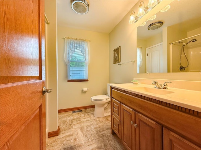 bathroom with baseboards, toilet, a shower, vanity, and stone finish flooring