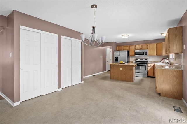 881 Sara Beth Ct, Saint Peters, MO 63376 - kitchen with stainless steel appliances, a kitchen island, a chandelier, light countertops, and brown cabinets