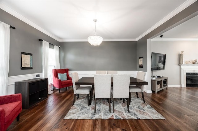 dining space featuring ornamental molding, wood finished floors, a chandelier, a wainscoted wall, and a fireplace
