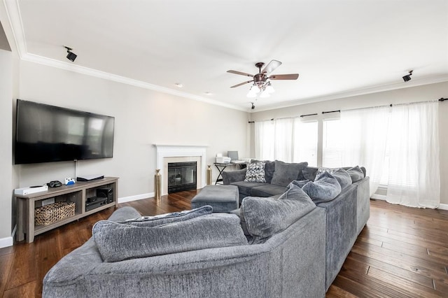 living room featuring a ceiling fan, ornamental molding, a fireplace, baseboards, and dark wood-style flooring