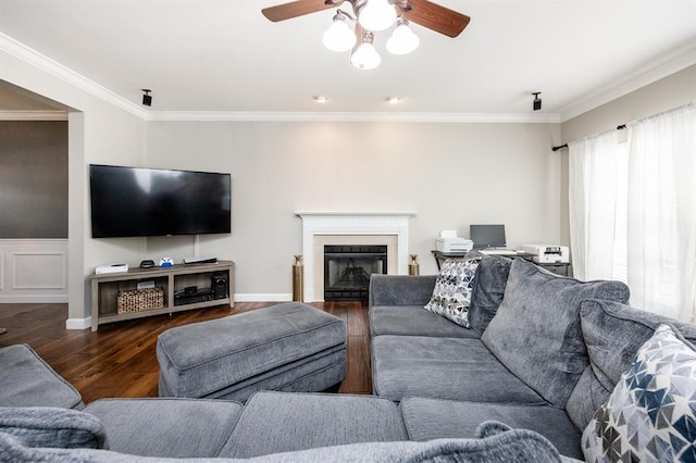 living room with wood finished floors, ceiling fan, ornamental molding, and a fireplace