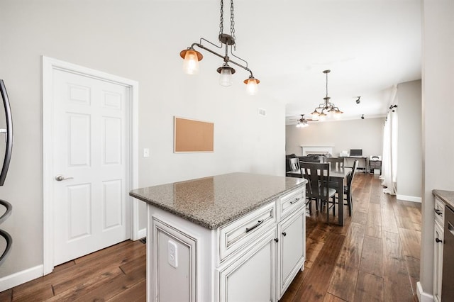 kitchen with dark wood-type flooring, hanging light fixtures, stone counters, and a center island