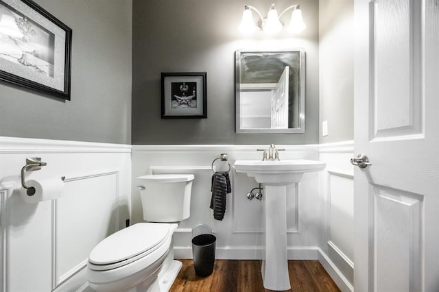 bathroom with toilet, wood finished floors, a wainscoted wall, and a decorative wall
