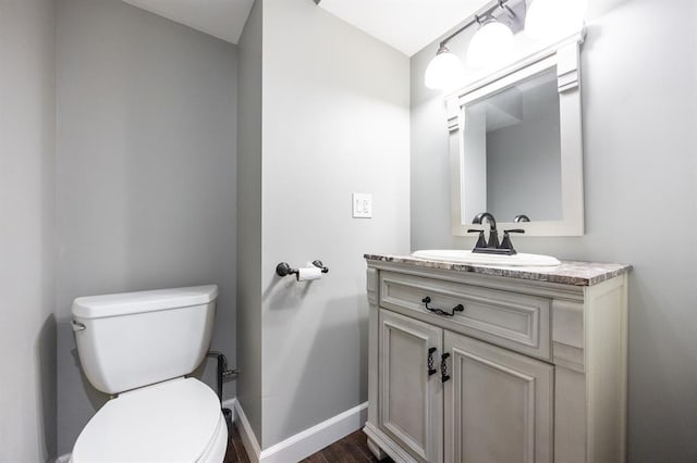 half bathroom with baseboards, toilet, vanity, and wood finished floors
