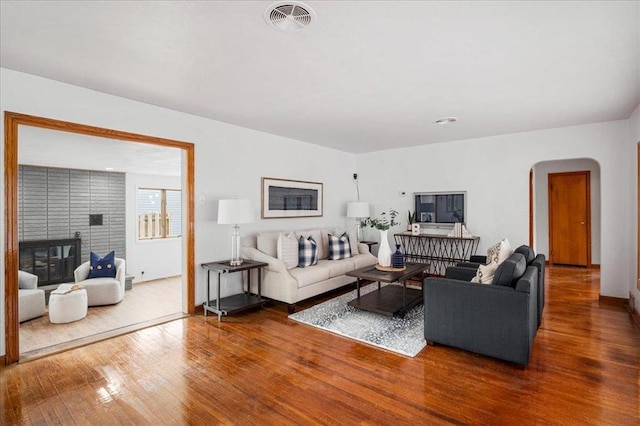 living room featuring arched walkways, wood finished floors, a fireplace, and baseboards