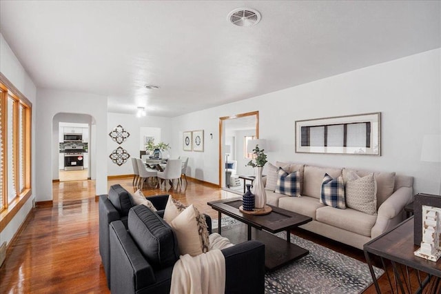 living area featuring arched walkways, wood finished floors, and baseboards