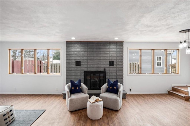 living room featuring wood finished floors, baseboards, a brick fireplace, recessed lighting, and a textured ceiling