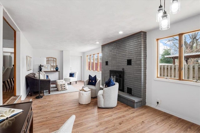 living area featuring a brick fireplace, healthy amount of natural light, baseboards, wood finished floors, and recessed lighting