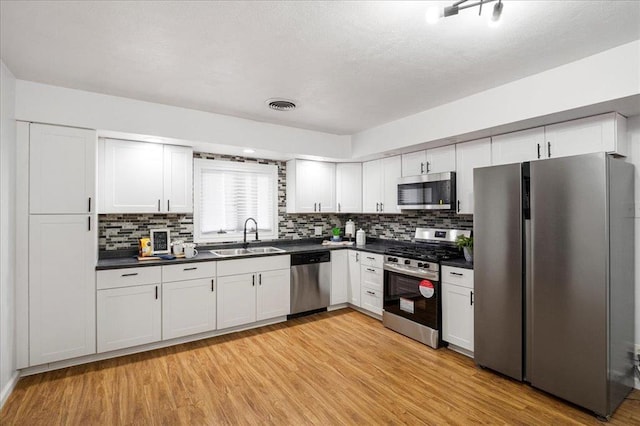 kitchen with appliances with stainless steel finishes, a sink, dark countertops, and decorative backsplash