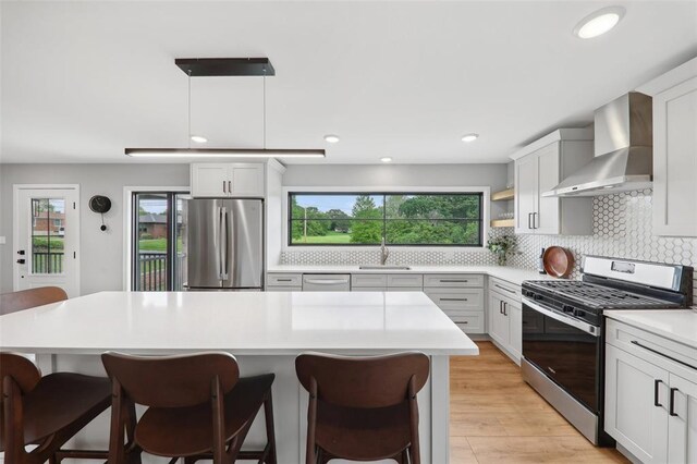 527 W Lake Dr, Edwardsville, IL 62025 - kitchen featuring appliances with stainless steel finishes, wall chimney range hood, a breakfast bar area, light countertops, and tasteful backsplash