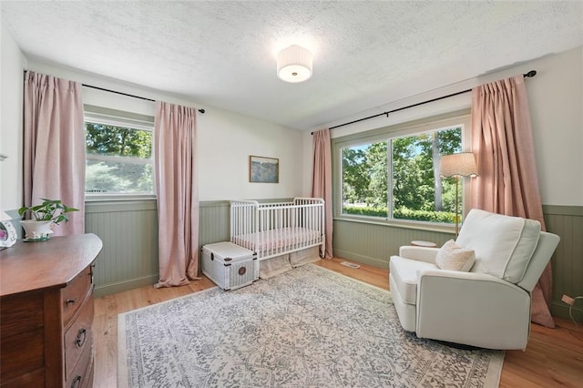 636 Parker Dr, Ballwin, MO 63021 - bedroom with light wood-style flooring, a textured ceiling, a nursery area, and wainscoting