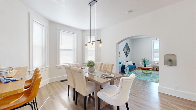 dining space with arched walkways, light wood-style floors, healthy amount of natural light, and baseboards