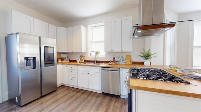kitchen featuring appliances with stainless steel finishes, a sink, island exhaust hood, wooden counters, and light wood-style floors