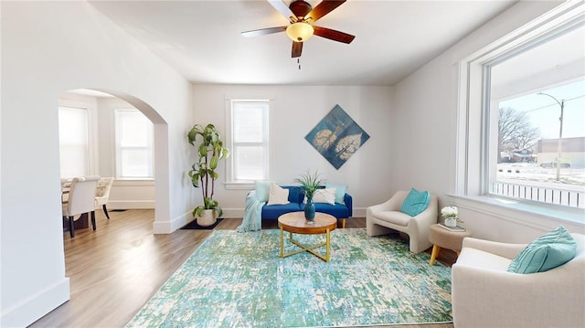 living area featuring arched walkways, wood finished floors, ceiling fan, and baseboards
