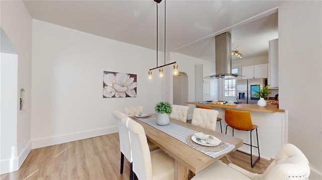 dining space featuring arched walkways, light wood-style floors, and baseboards