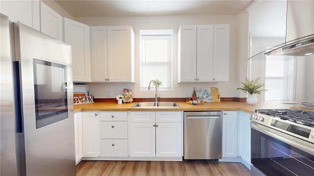 kitchen featuring appliances with stainless steel finishes, a sink, extractor fan, white cabinetry, and light wood-style flooring