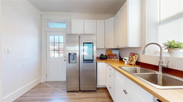 kitchen with stainless steel fridge, a sink, white cabinetry, and light countertops