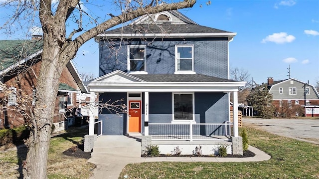 american foursquare style home with covered porch, brick siding, and a front lawn