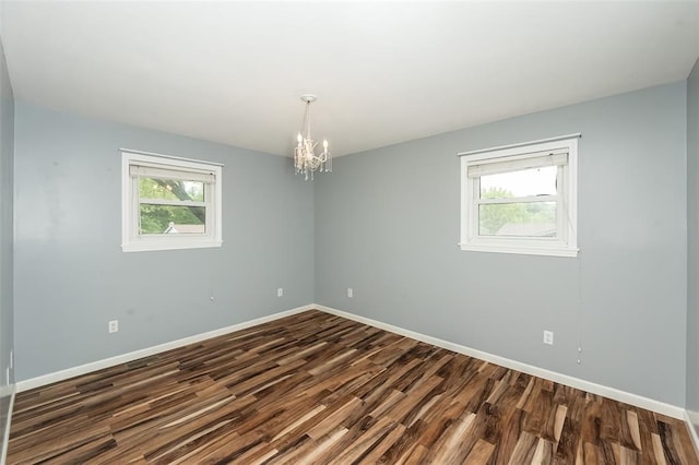 unfurnished room with dark wood-style flooring, plenty of natural light, a chandelier, and baseboards