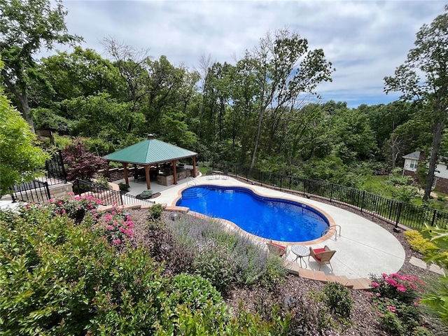 view of swimming pool featuring a gazebo, a patio, fence, and a wooded view