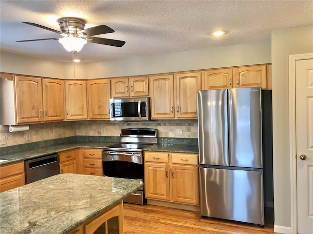 kitchen with stainless steel appliances, decorative backsplash, light wood finished floors, dark stone counters, and a textured ceiling