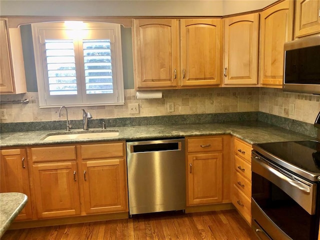 kitchen featuring stainless steel appliances, a sink, backsplash, and wood finished floors