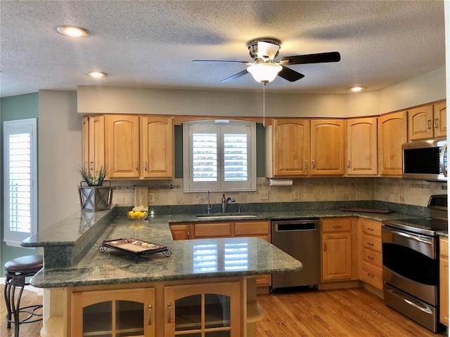 kitchen featuring stainless steel appliances, a sink, a kitchen breakfast bar, a peninsula, and backsplash