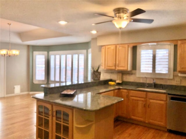 kitchen featuring stainless steel dishwasher, a sink, a peninsula, light wood-style floors, and decorative light fixtures