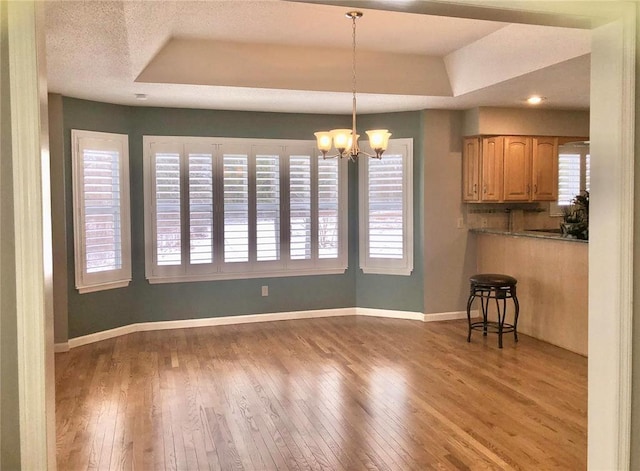 unfurnished dining area featuring a tray ceiling, hardwood / wood-style flooring, baseboards, and a chandelier