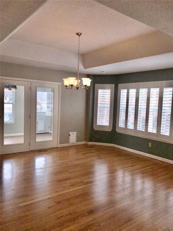 empty room featuring wood finished floors, a chandelier, baseboards, a textured ceiling, and a raised ceiling