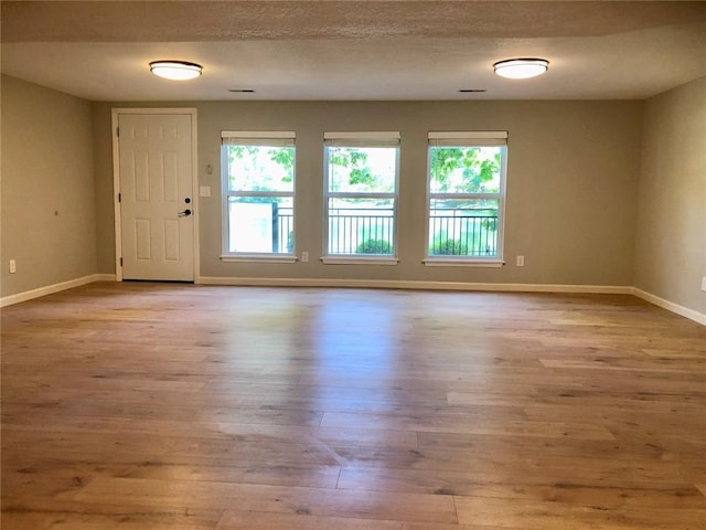 unfurnished room with wood finished floors, plenty of natural light, baseboards, and a textured ceiling