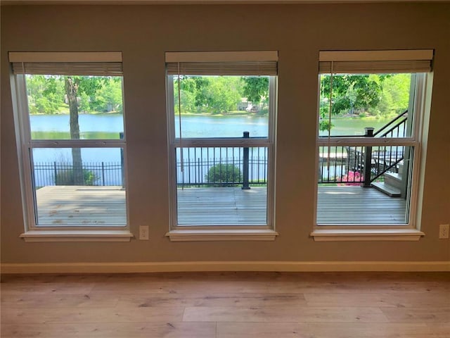 doorway with baseboards, a water view, and light wood-style floors