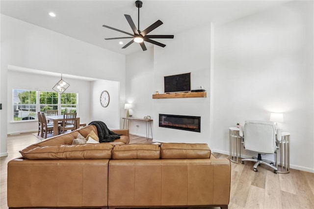 1513 Grey Wolf Dr, Imperial, MO 63052 - living room featuring a ceiling fan, light wood-style flooring, a glass covered fireplace, baseboards, and a towering ceiling