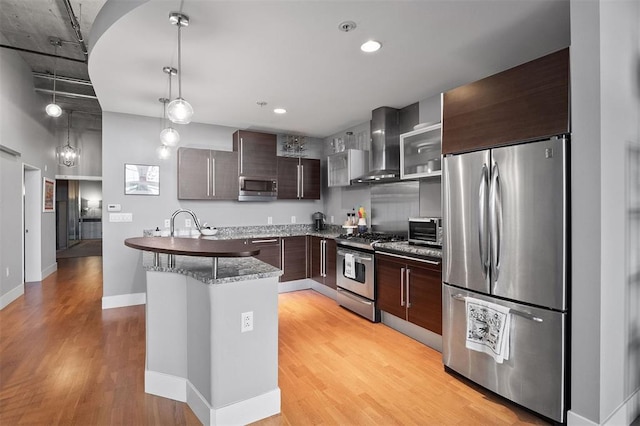4100 Forest Park Ave Unit 323, Saint Louis, MO 63108 - kitchen with stainless steel appliances, wall chimney exhaust hood, light wood-style floors, dark brown cabinetry, and pendant lighting