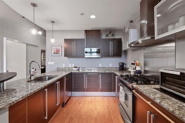 4100 Forest Park Ave Unit 323, Saint Louis, MO 63108 - kitchen featuring appliances with stainless steel finishes, wall chimney exhaust hood, a sink, light wood-type flooring, and pendant lighting
