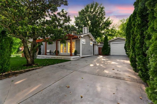 view of property hidden behind natural elements featuring an outdoor structure, a garage, a chimney, and concrete driveway