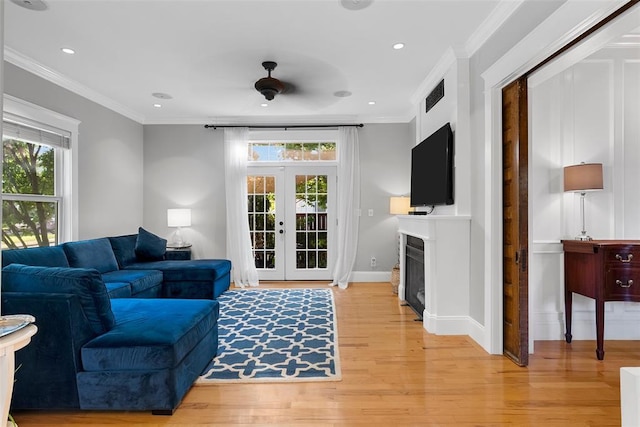 living room with french doors, light wood-style floors, recessed lighting, crown molding, and a fireplace
