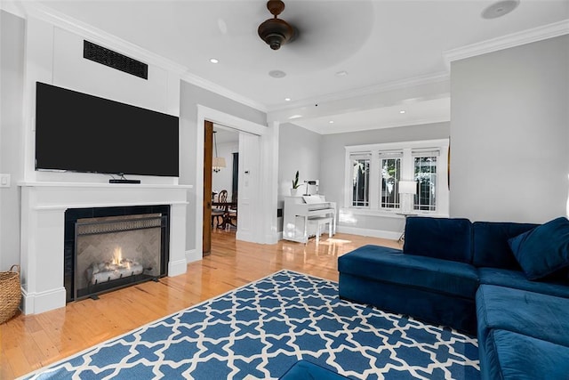 living room with wood finished floors, ornamental molding, a lit fireplace, recessed lighting, and ceiling fan