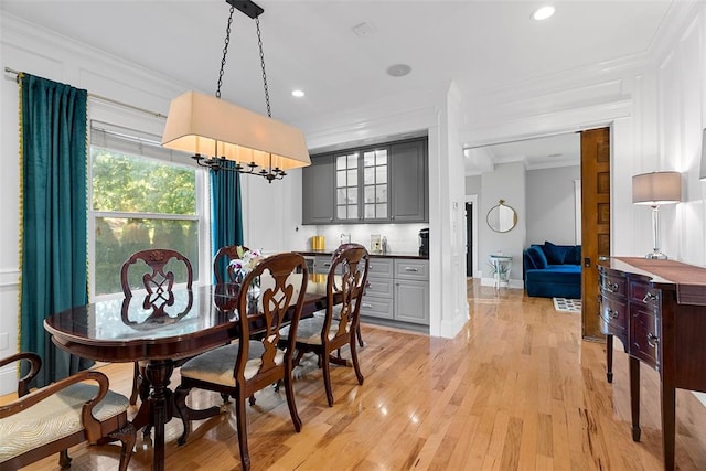 dining room featuring crown molding, light wood-type flooring, bar area, baseboards, and recessed lighting
