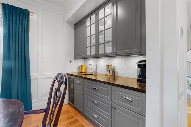 bar featuring a sink, backsplash, ornamental molding, beverage cooler, and light wood-type flooring