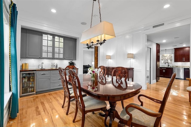 dining room with beverage cooler, bar with sink, crown molding, light wood-type flooring, and recessed lighting